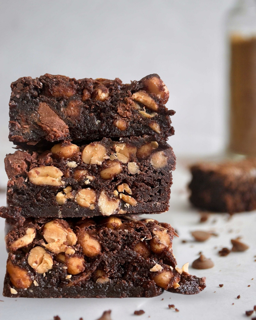 Stack of three brownies with visible chocolate chunks and peanuts on a light background.