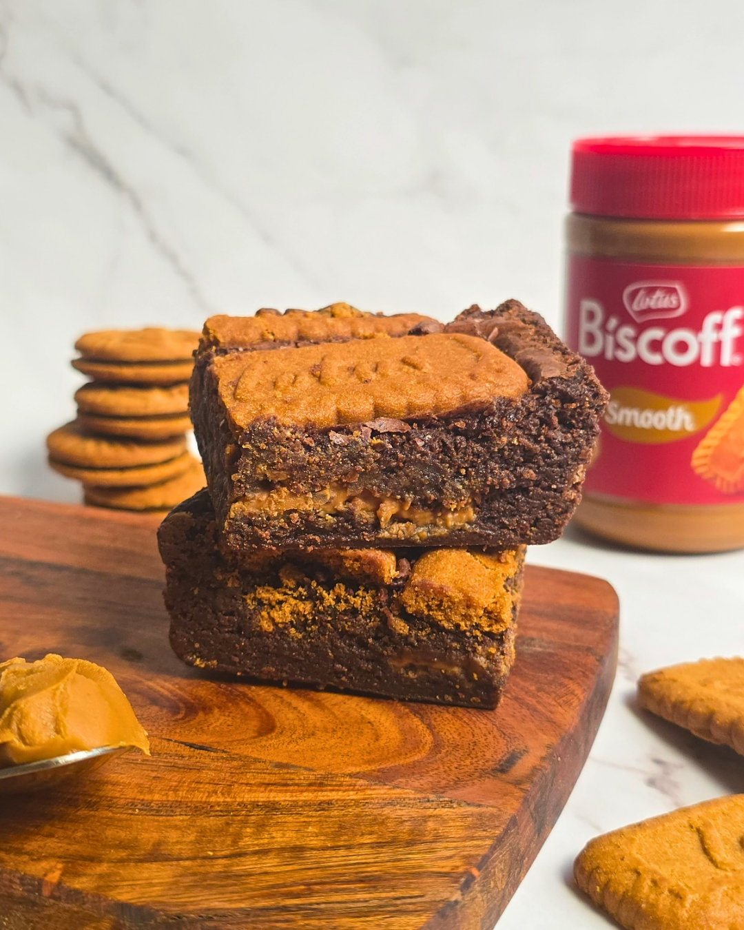 Stacked Biscoff brownies on a wooden board with Biscoff cookies and a jar of Biscoff spread in the background.