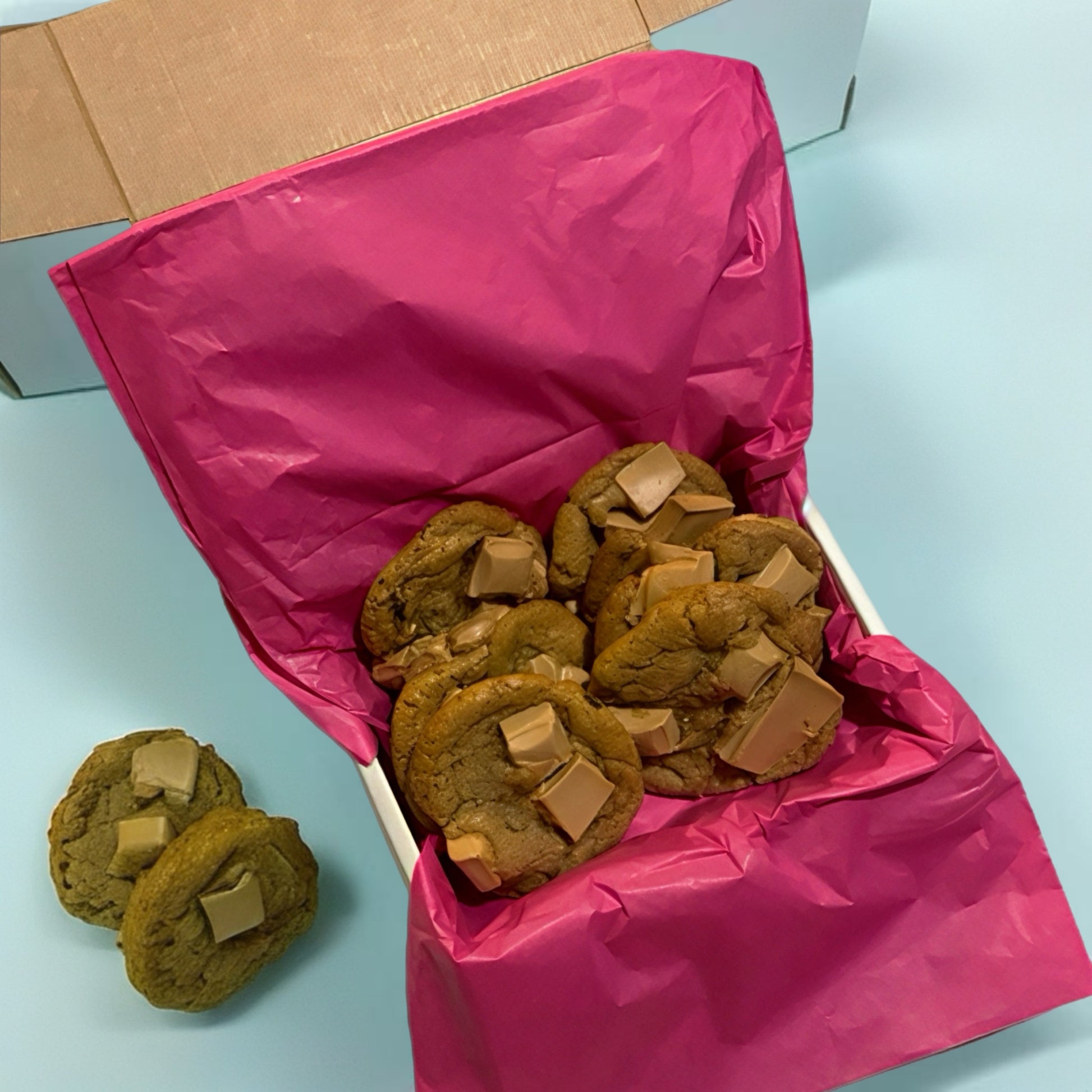 Box of cookies with pink tissue paper on a light blue background