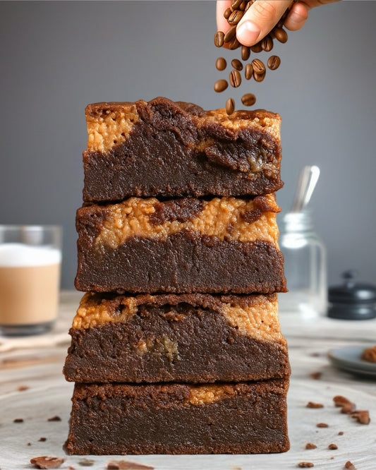 Stack of brownies with a hand sprinkling coffee beans on top, with a blurred background.