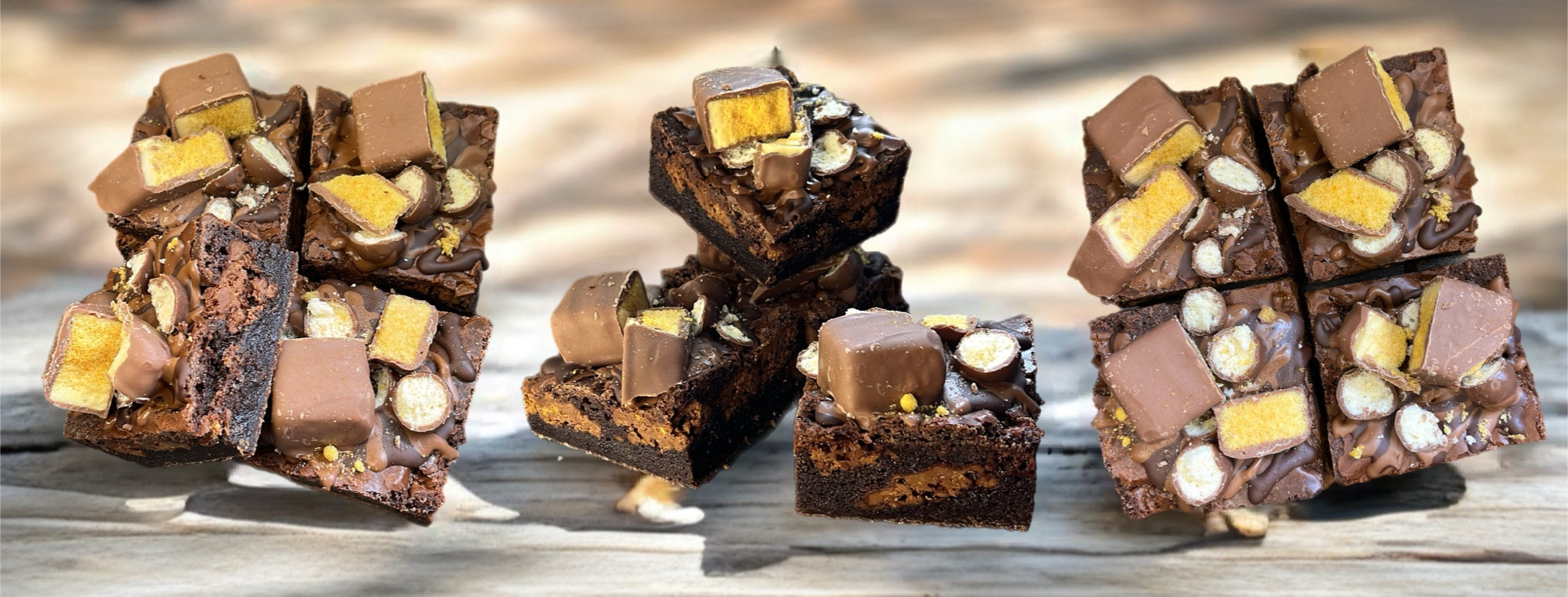 Four stacks of assorted chocolate and Hokey Pokey candy bar brownies on a wooden surface. 
